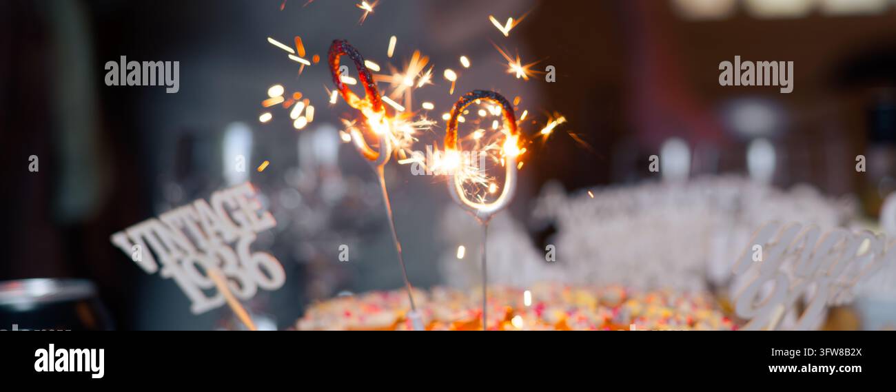 Candele scintillanti numero 90 che bruciano luminose su una torta, per celebrare una festa di 80° compleanno con tema vintage Foto Stock