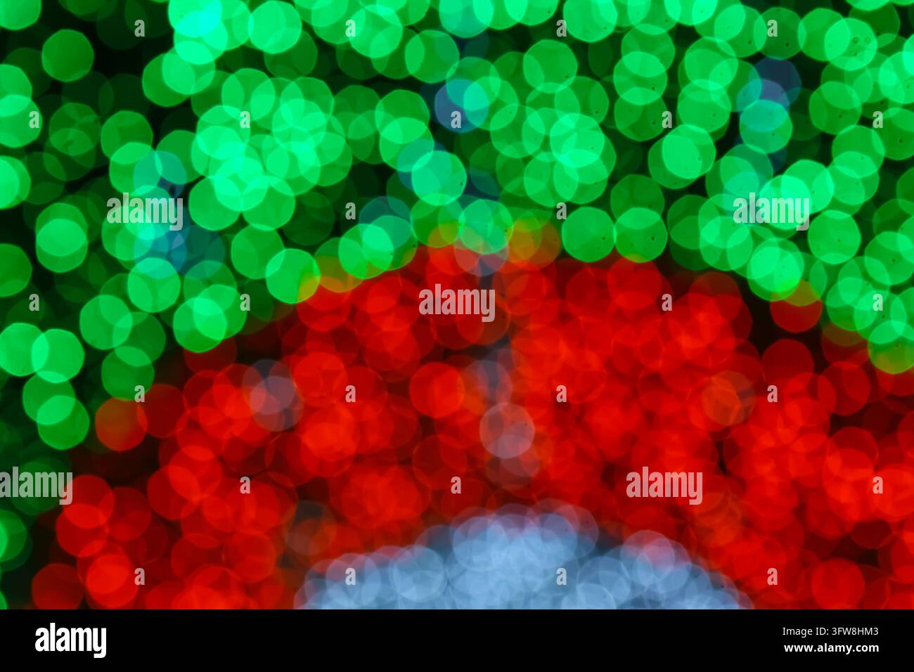 Luci bokeh natalizie astratte in verde, rosso, bianco e blu formano cerchi stratificati su uno sfondo scuro in Thailandia, adatte per il design delle festività. Foto Stock
