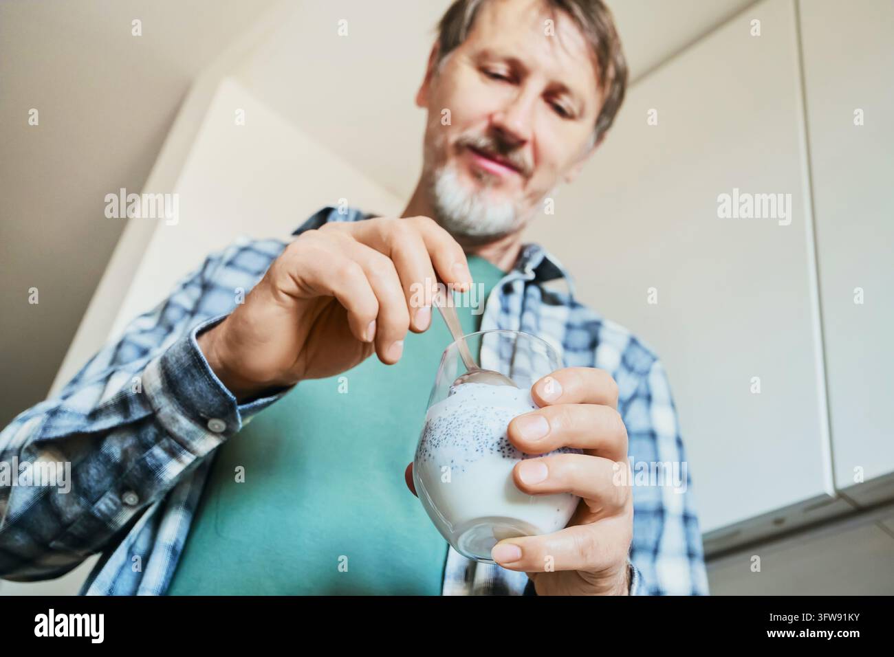 Prima piano di un uomo maturo che mescola semi di chia nel latte con un cucchiaio per una nutrizione sana Foto Stock