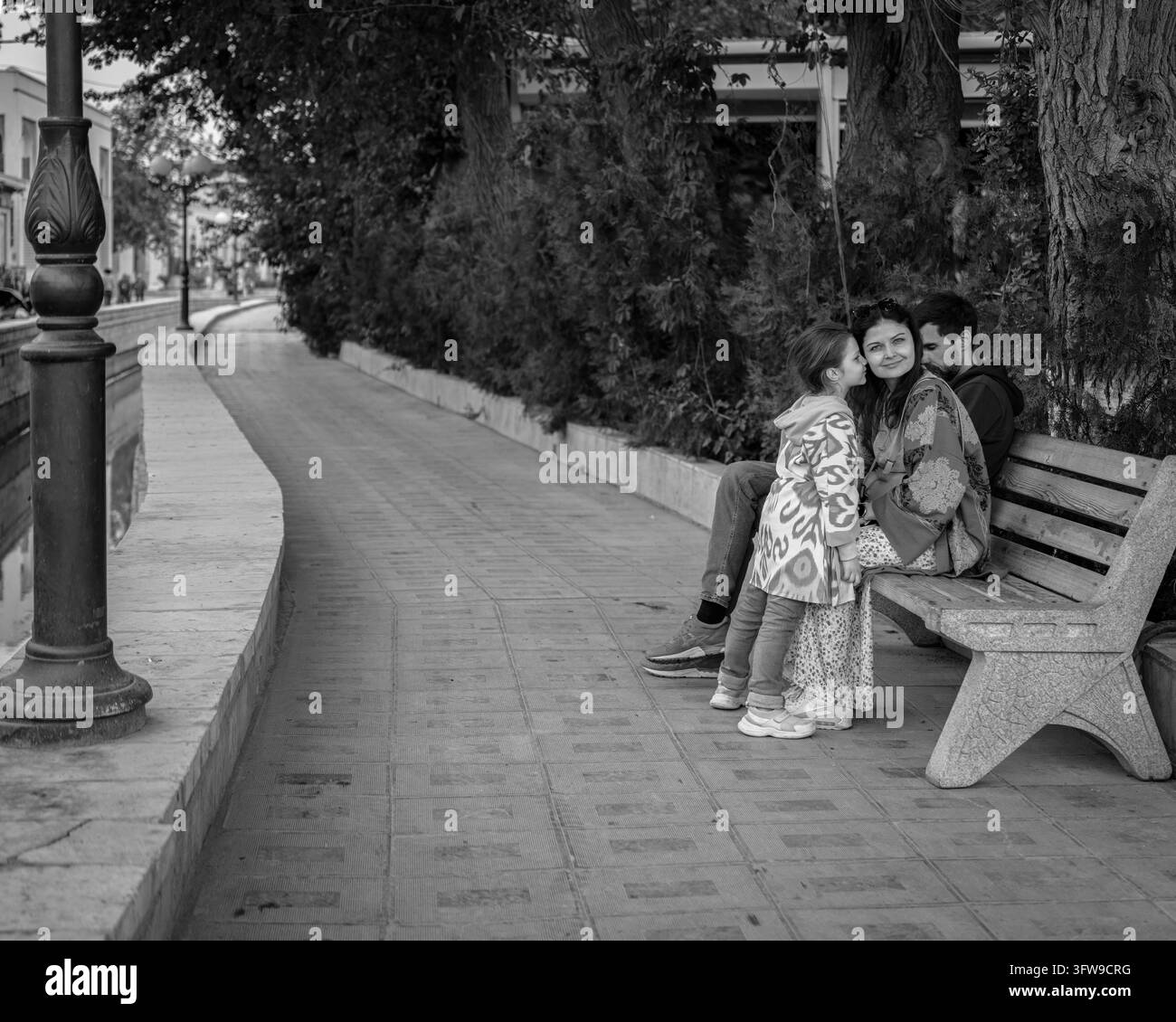 Due persone sedute insieme su una panchina accanto a un viale alberato a Bukhara, Uzbekistan. Foto Stock