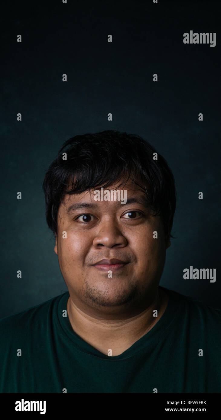 Un ritratto frontale presenta un modello maschile asiatico adulto che guarda direttamente nella lente della fotocamera con un sorriso sottile e amichevole. Questo individuo indossa un sim Foto Stock
