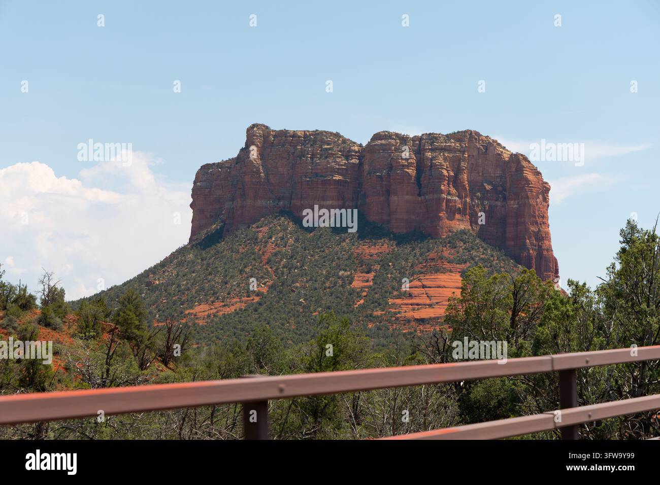 Vista di Courthouse Butte sopra una ringhiera in legno, con foresta di ginepri sottostante e un cielo blu con nuvole sopra, nella terra delle rocce rosse di Sedona, Ari Foto Stock