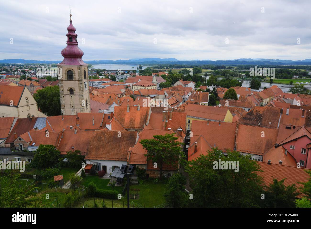 Vista elevata sui tetti con tegole rosse e sulla chiesa di San Giorgio verso il fiume Drava nella storica città di Ptuj, in Slovenia. Foto Stock