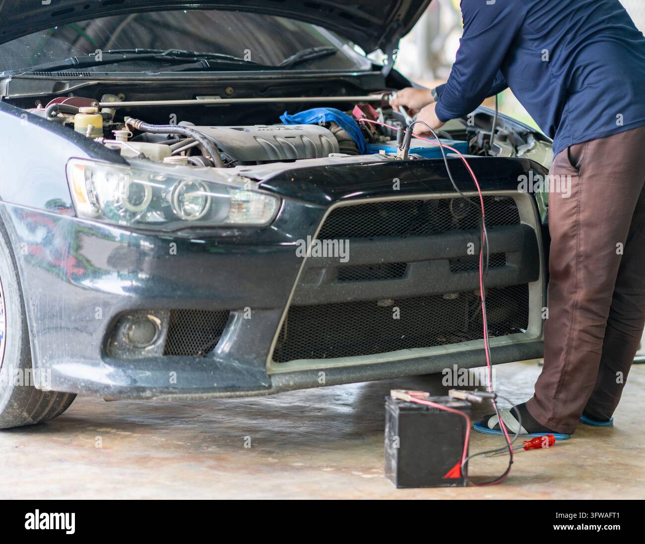 Tecnico professionista che effettua la manutenzione di un motore di auto e carica la batteria con pinze di salvataggio in un'officina di riparazione auto. Foto Stock