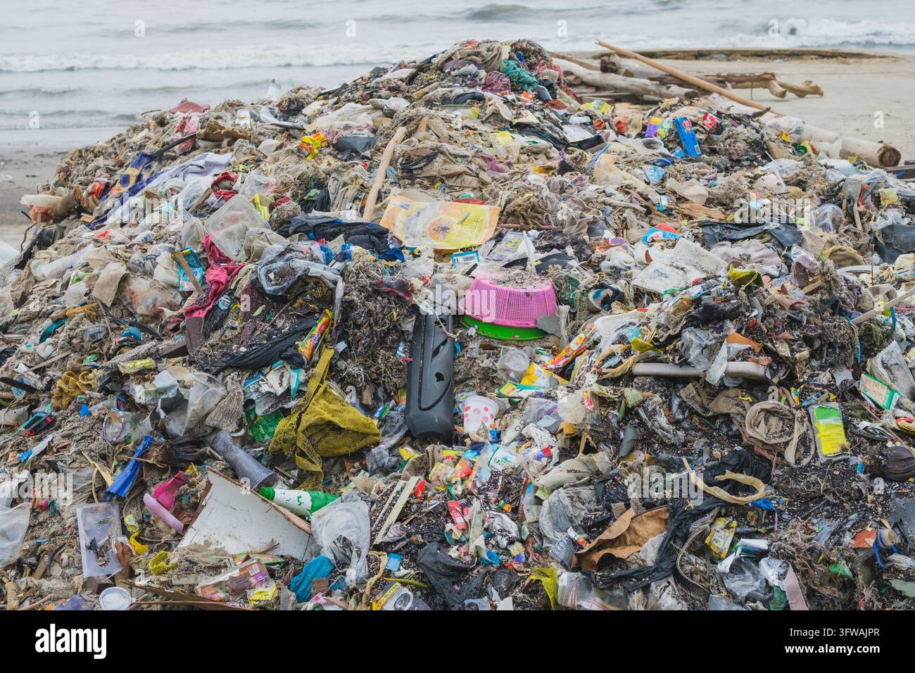 Balikpapan, Indonesia - 16 ottobre 2026. Un enorme cumulo di rifiuti misti, immondizia e plastica spinti da un'onda su una spiaggia sabbiosa affacciata sull'oceano. Foto Stock