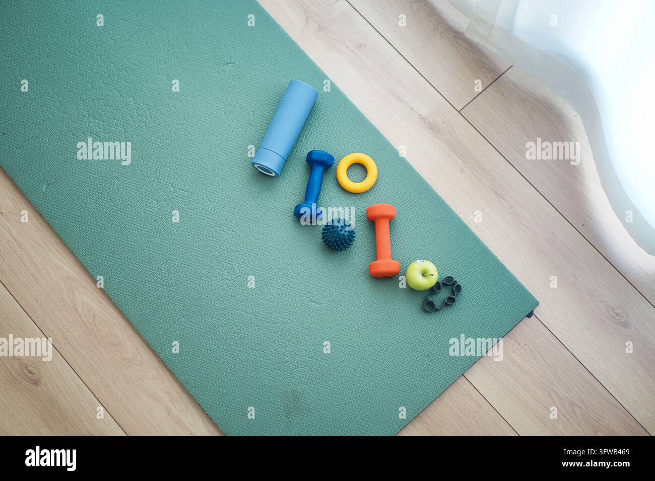 Pesi per esercizi e rulli da massaggio disposti su un tappeto da yoga al chiuso Foto Stock