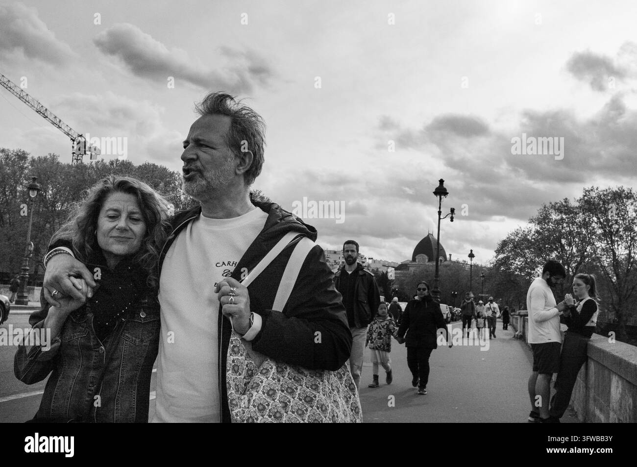 COPPIA FELICE CHE PASSEGGIA IN CITTÀ, REPORTAGE DELLA DOMENICA SULLA RIVA SINISTRA DELLA SENNA, PARIGI, FRANCIA, 2026: Una coppia sorridente di mezza età cammina a braccetto lungo un marciapiede affollato sotto un cielo nuvoloso. INFO: La Rive Gauche a est di Notre-Dame unisce eredità accademica e romanticismo fluviale. Passeggiare davanti alle università storiche, ai tranquilli giardini botanici e al moderno Istituto del Mondo Arabo rivela un angolo vivace e meno turistico di Parigi, che pulsa di anima intellettuale. Foto Stock