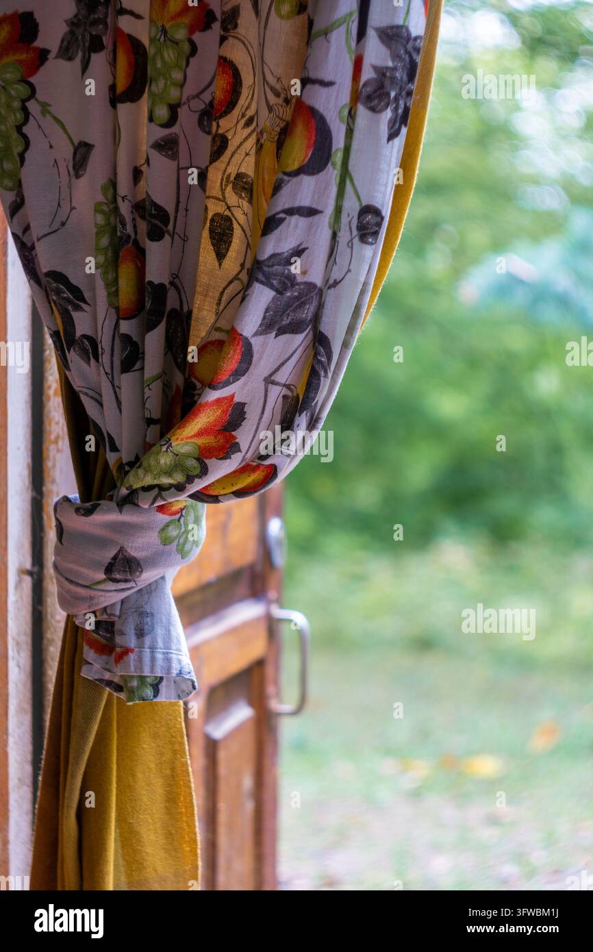 Una bella tenda con frutti dipinti è annodata alla fine nel passaggio. Porta di legno aperta e alberi sullo sfondo Foto Stock