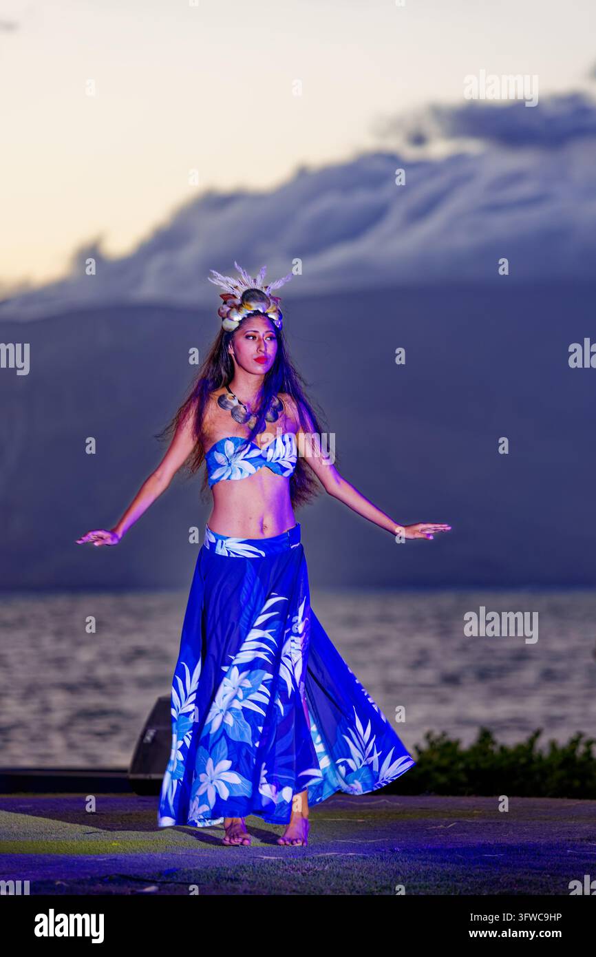 Ballerina polinesiana in una gonna floreale blu e copricapo di conchiglie che si esibisce a un luau al crepuscolo, Wailea, Maui, Hawaii Foto Stock