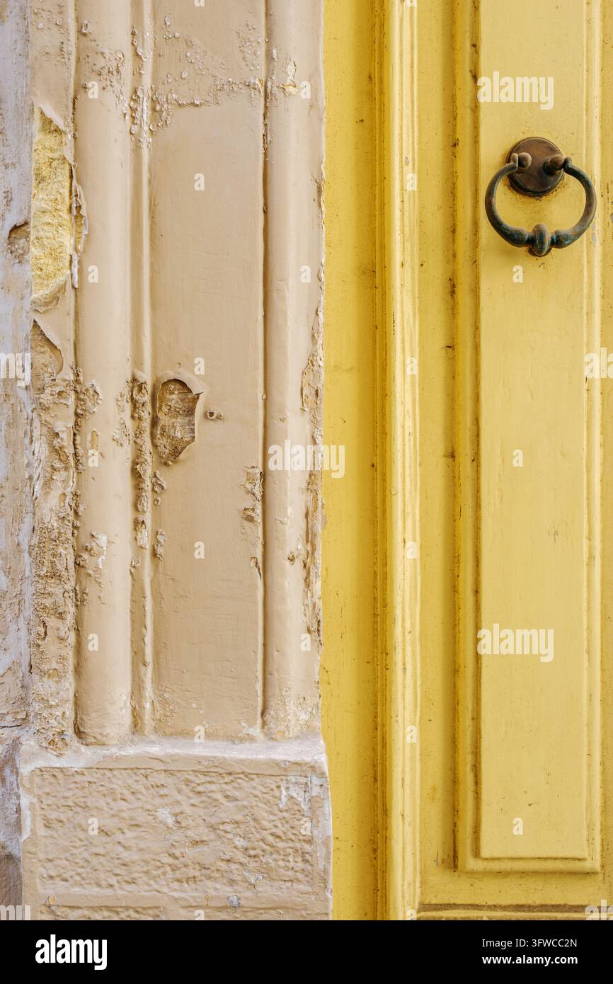 Porta in legno gialla con batacchio in metallo antico e muro in pietra consumato, intonaco logoro e superfici ruvide Foto Stock