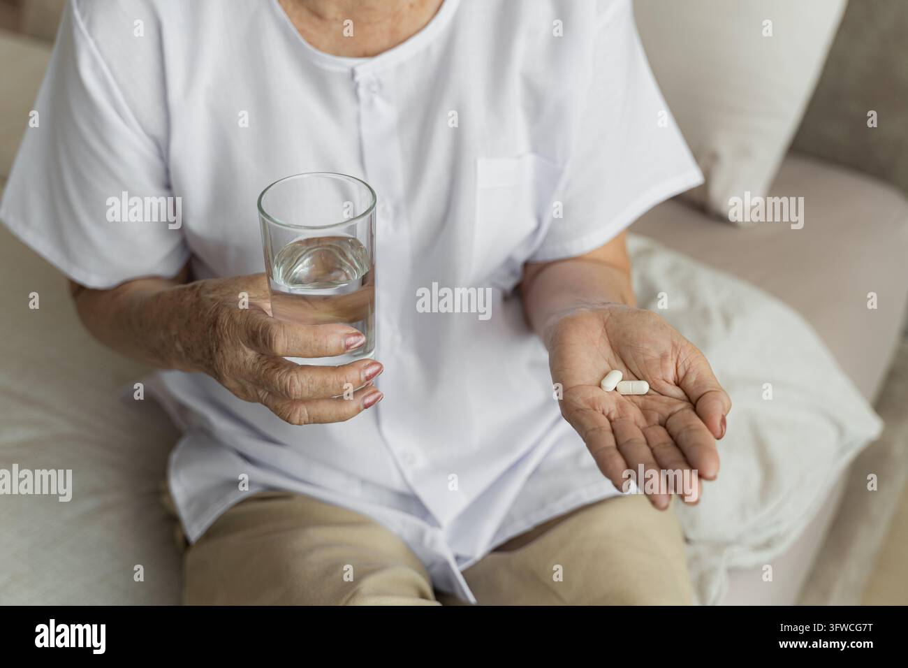Una donna anziana sta prendendo farmaci con un bicchiere d'acqua a casa come parte della sua routine di benessere. Ideale per l'assistenza sanitaria, le residenze per anziani e il benessere Foto Stock