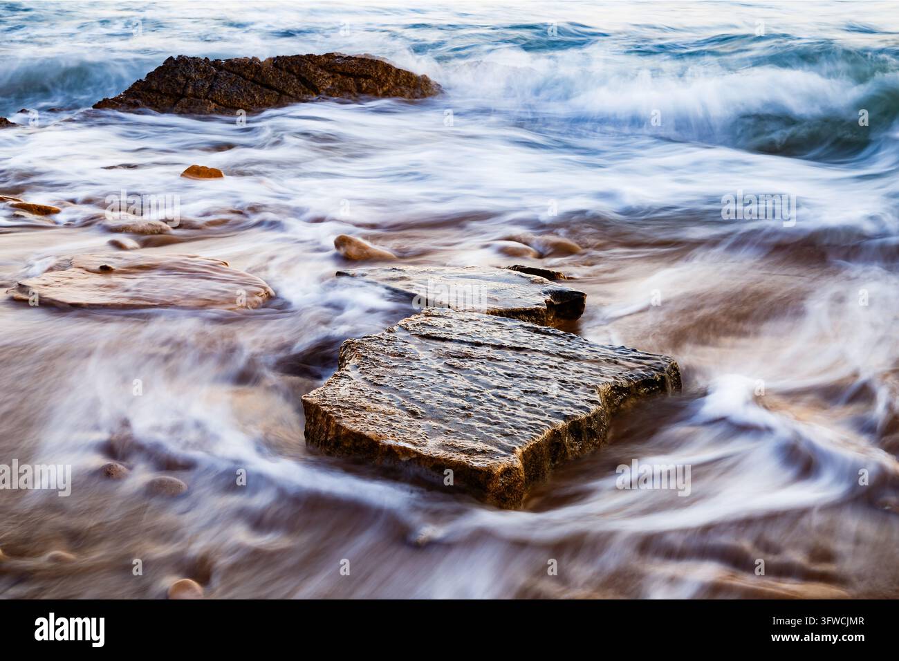 Schiuma oceanica che turbina sui roccioli della spiaggia di Villajoyosa Foto Stock