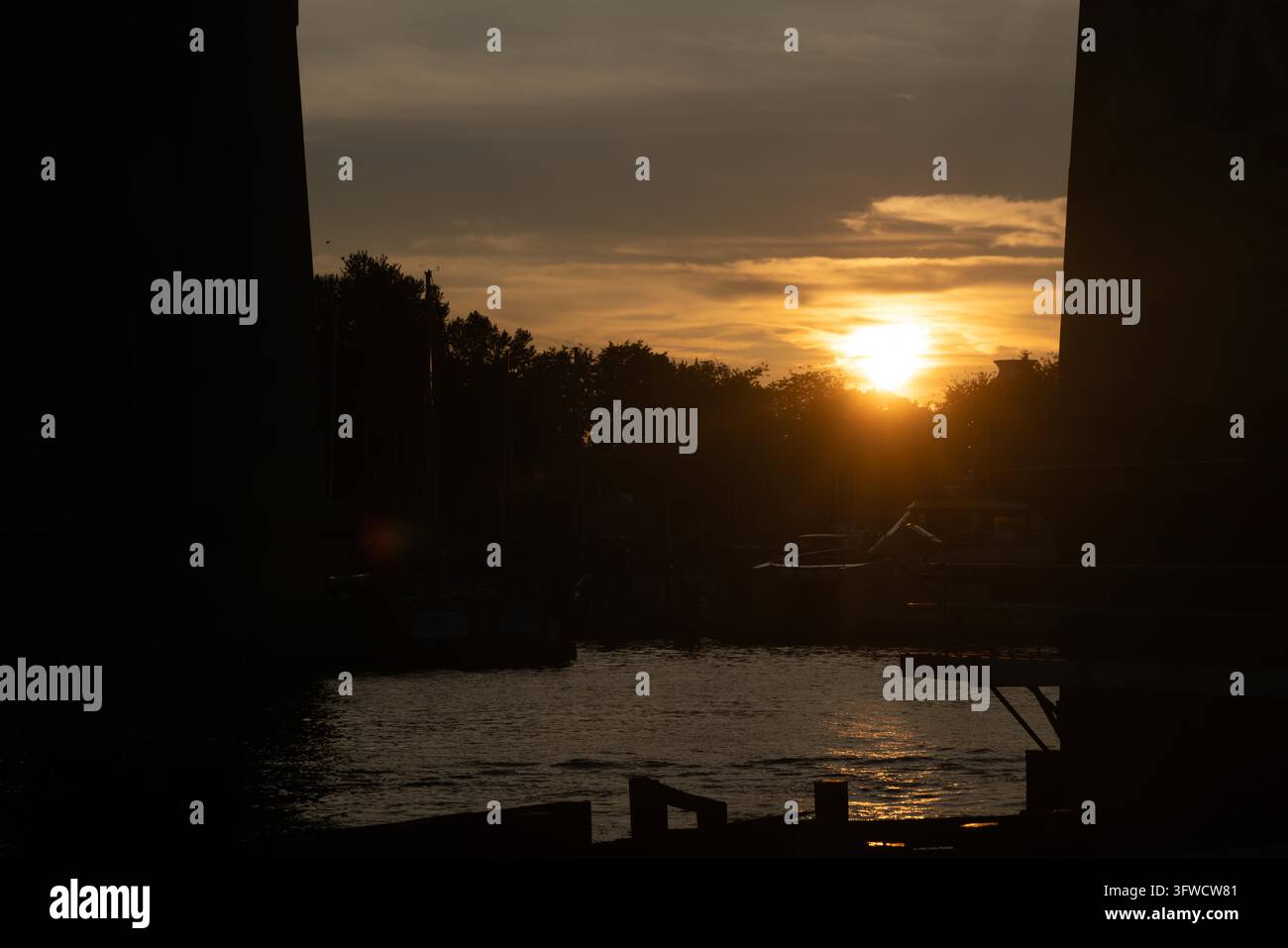 Vancouver, Canada, Prospettiva orizzontale sull'acqua che guarda oltre i pilastri scuri del ponte verso il sole brillante che tramonta e si riflette sulle acque del porto. Foto Stock