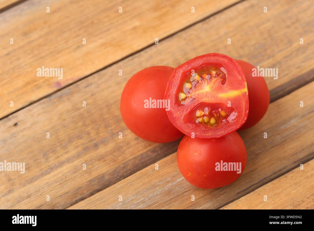 Fresche pomodorini rossi biologici interi e a metà su un tavolo di legno. Foto Stock