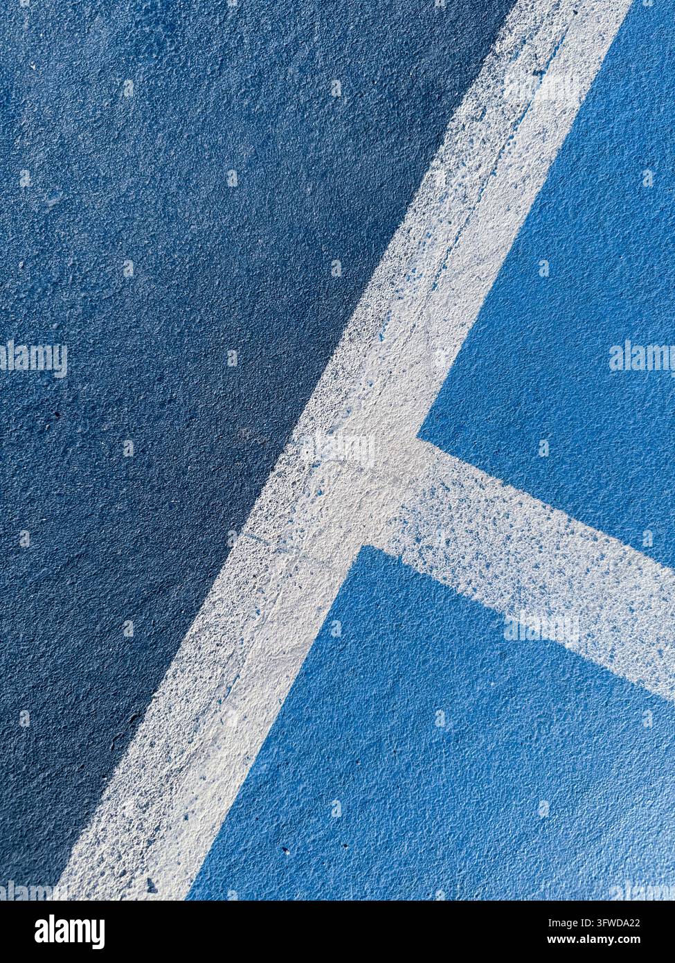 Superficie blu strutturata da campo sportivo con linee bianche intersecanti che creano confini chiari, formando schemi geometrici astratti Foto Stock