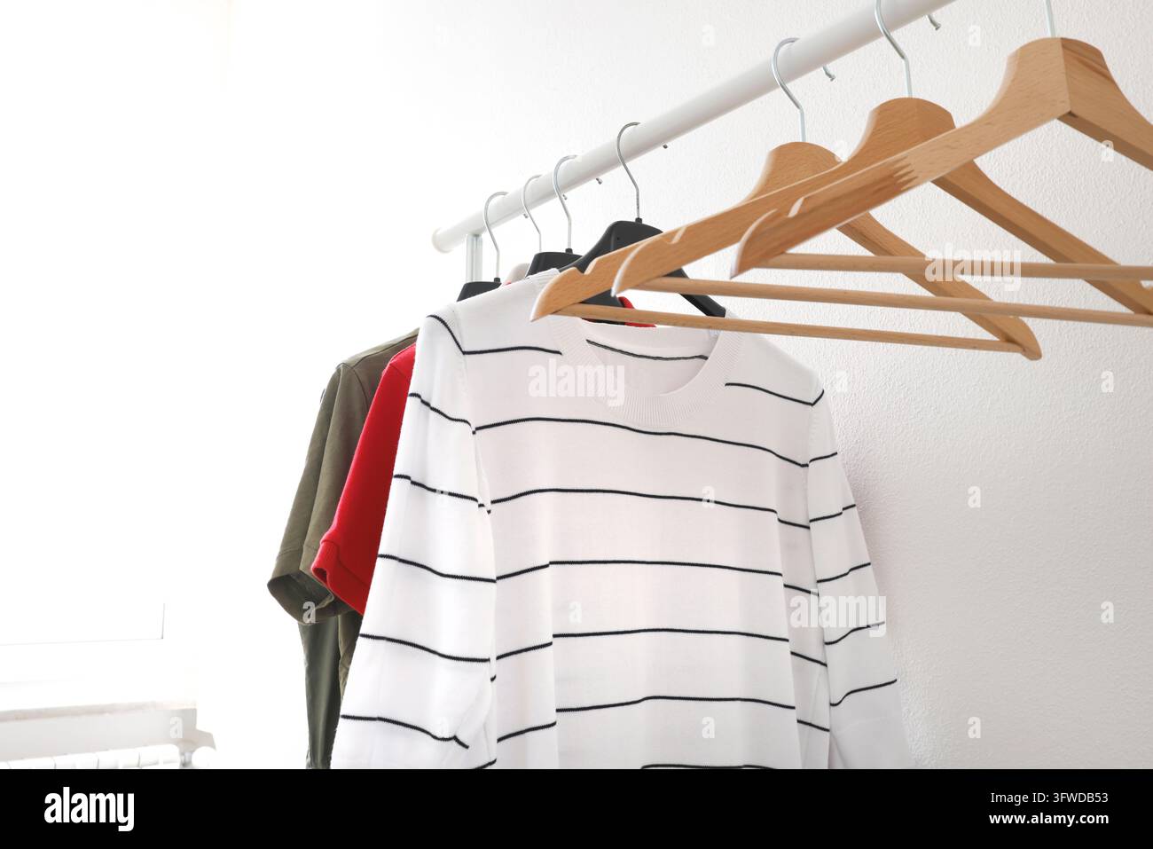 Modello di appendiabiti in legno vuoti su gruccia con magliette casual. Modello di branding estetico eco spazio di copia. Design di moda per guardaroba domestico Foto Stock