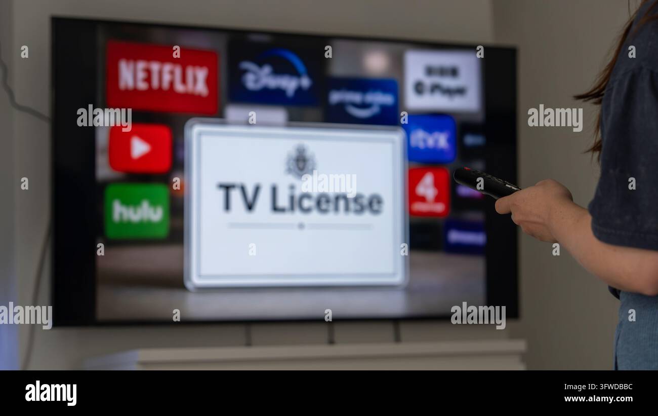 Una persona indica con un telecomando una smart TV che mostra icone di app di streaming e un messaggio di licenza TV, illustrando gli abbonamenti all'intrattenimento domestico e la televisione Foto Stock
