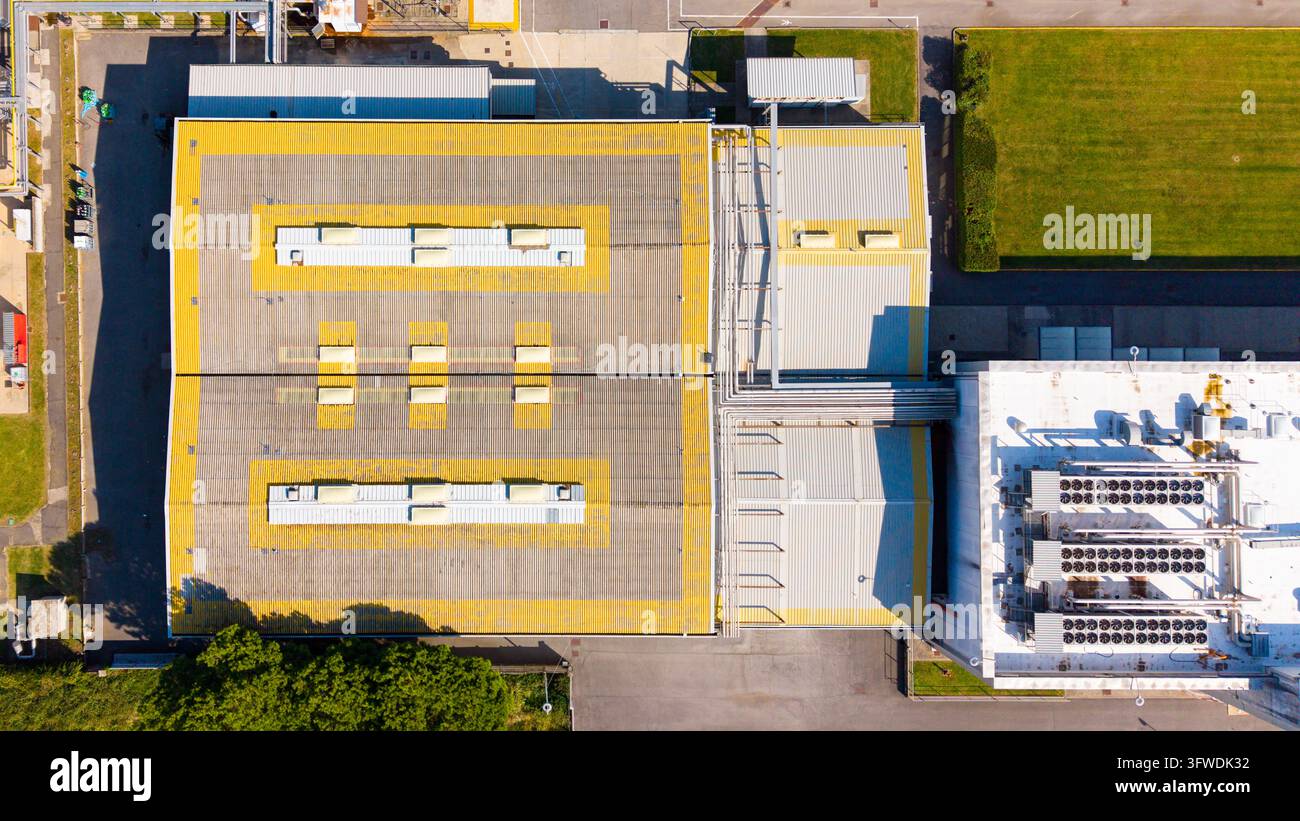 Veduta aerea di una struttura di un'azienda farmaceutica con un grande edificio industriale con segni gialli sul tetto, unità di ventilazione e vegetazione circostante Foto Stock