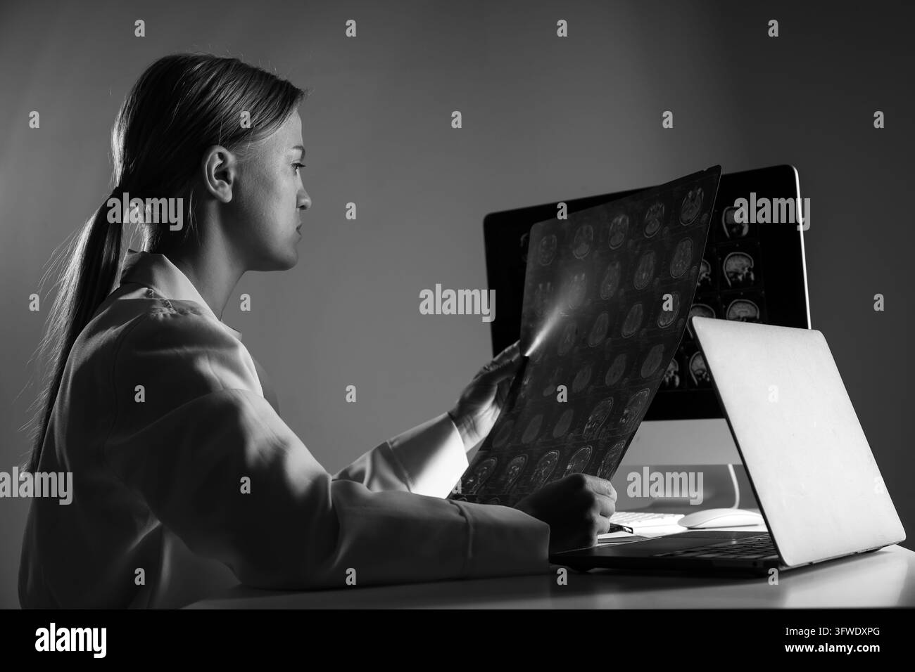 Una giovane dottoressa osserva un'immagine RM di una testa umana. Foto in bianco e nero Foto Stock