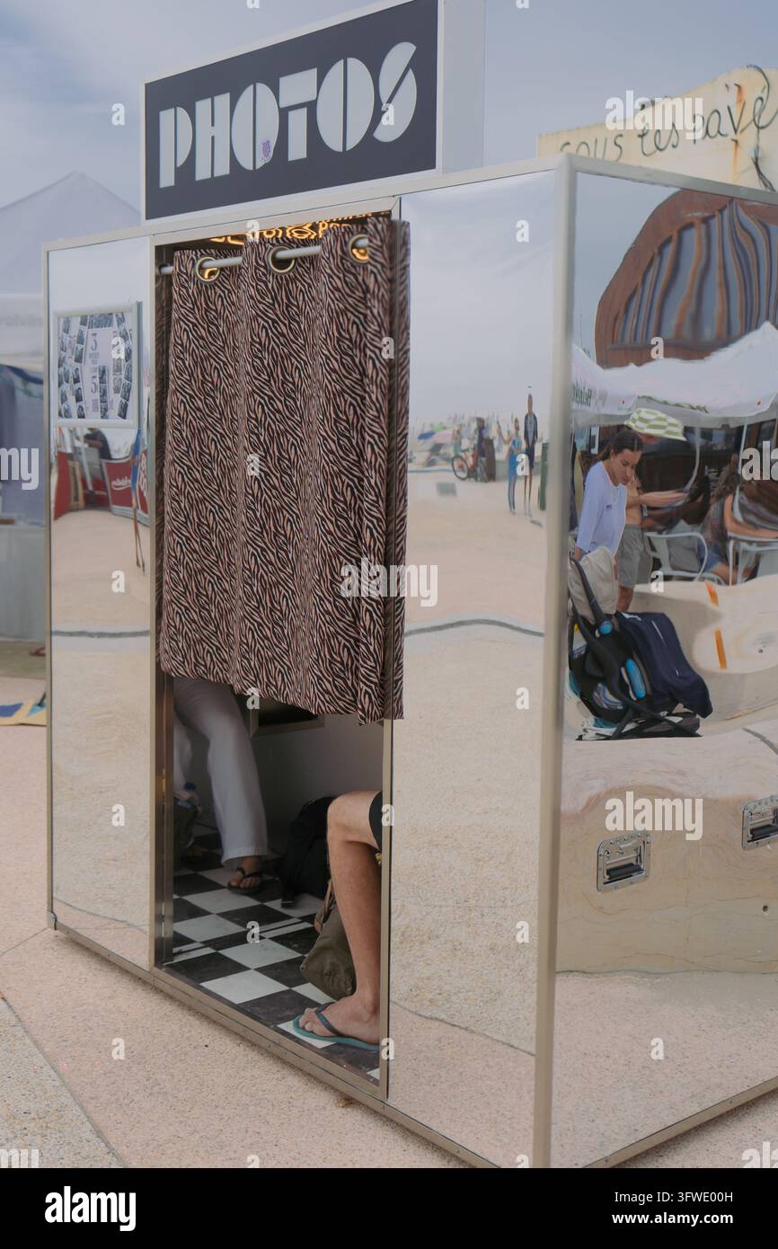 Cabina fotografica retrò in argento con la tenda chiusa, mentre le gambe delle persone all'interno sono visibili, in piedi all'aperto in una giornata estiva soleggiata. Foto Stock