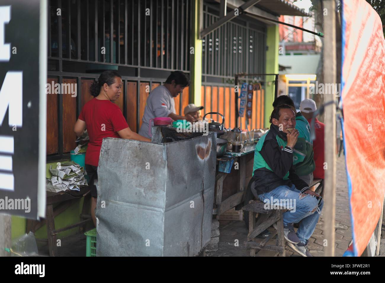 I venditori ambulanti preparano e servono cibo in un piccolo warung in un quartiere indonesiano. Foto Stock