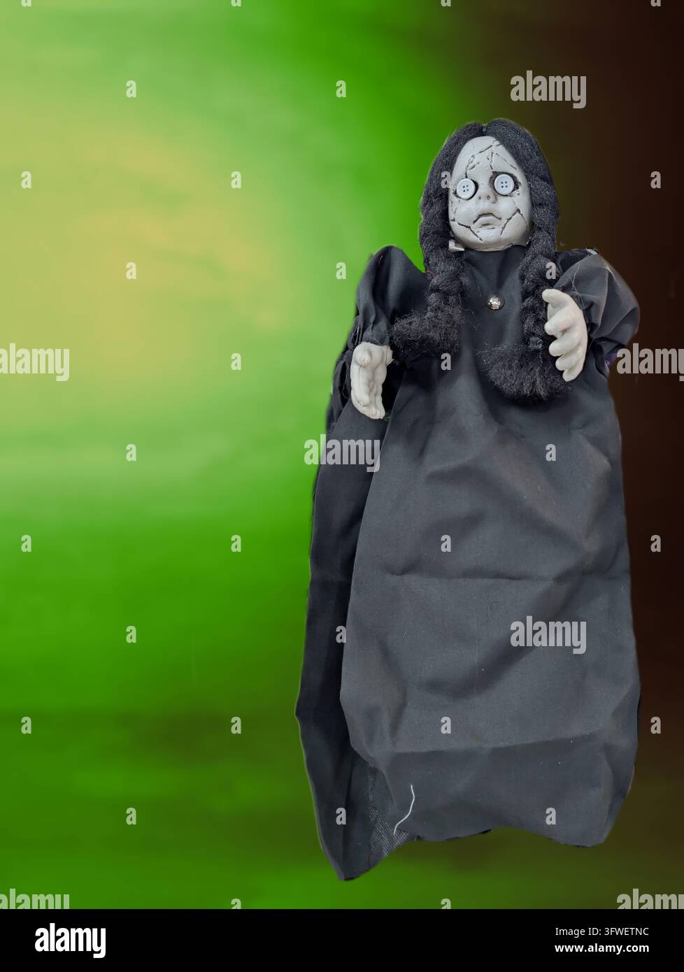 Un pupazzo nero con cappuccio, con un volto disegnato e mani pallide, è appeso contro uno sfondo verde, rivolto in avanti con le braccia alzate. Foto Stock