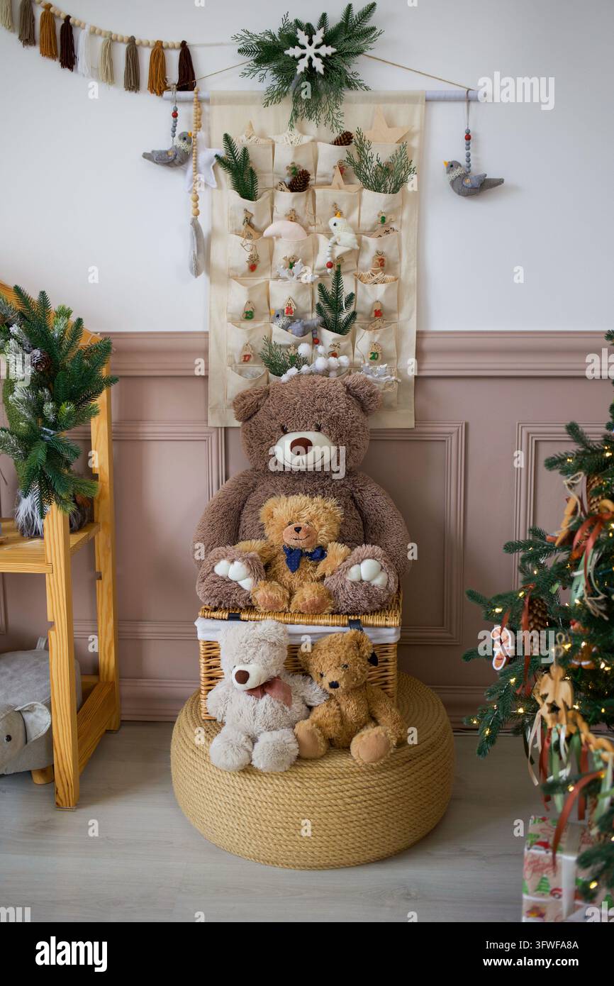 Famiglia di orsacchiotti di peluche seduta su un ottomana intrecciata con cassapanca in vimini e decorazione da parete con calendario dell'Avvento Foto Stock
