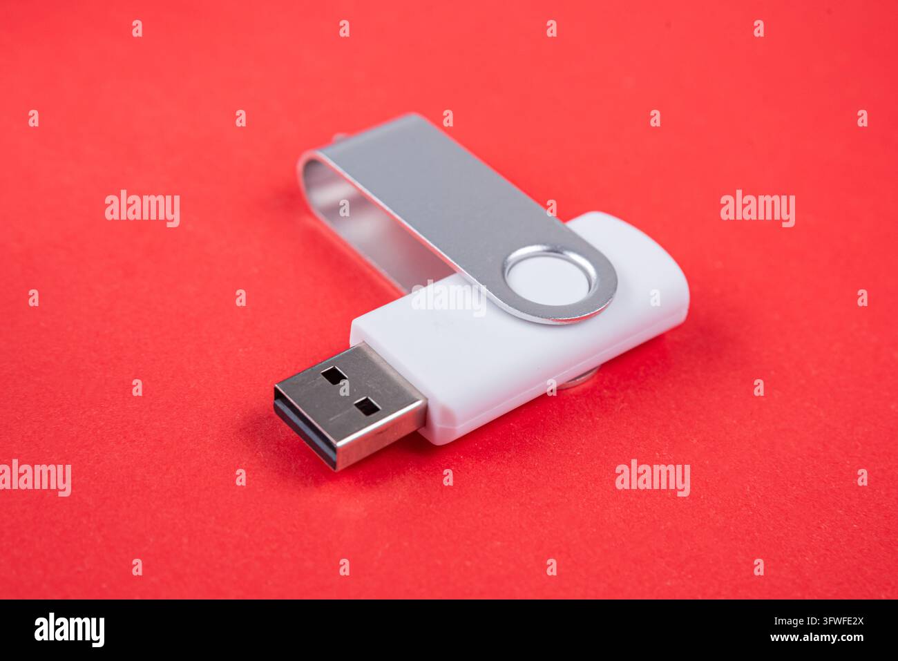 Una semplice chiavetta USB bianca con un cappuccio girevole in metallo argentato poggia su uno sfondo rosso vivace e texture, simboleggiando l'archiviazione digitale e il trasferimento di dati Foto Stock