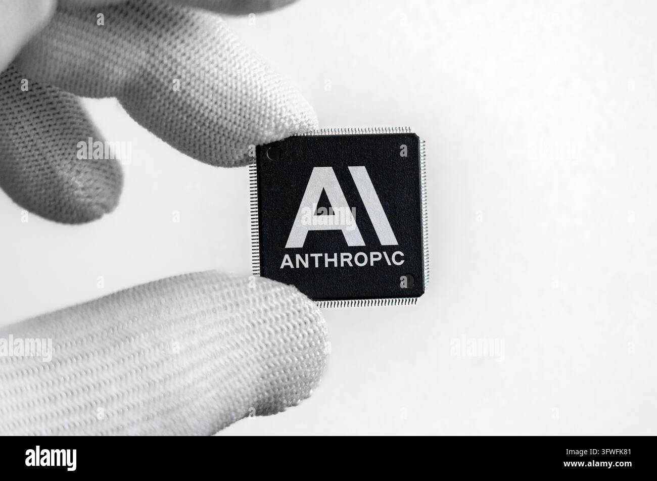 Prima piani di una persona che indossa un guanto bianco e tiene un microchip semiconduttore con il logo Anthropic AI Foto Stock