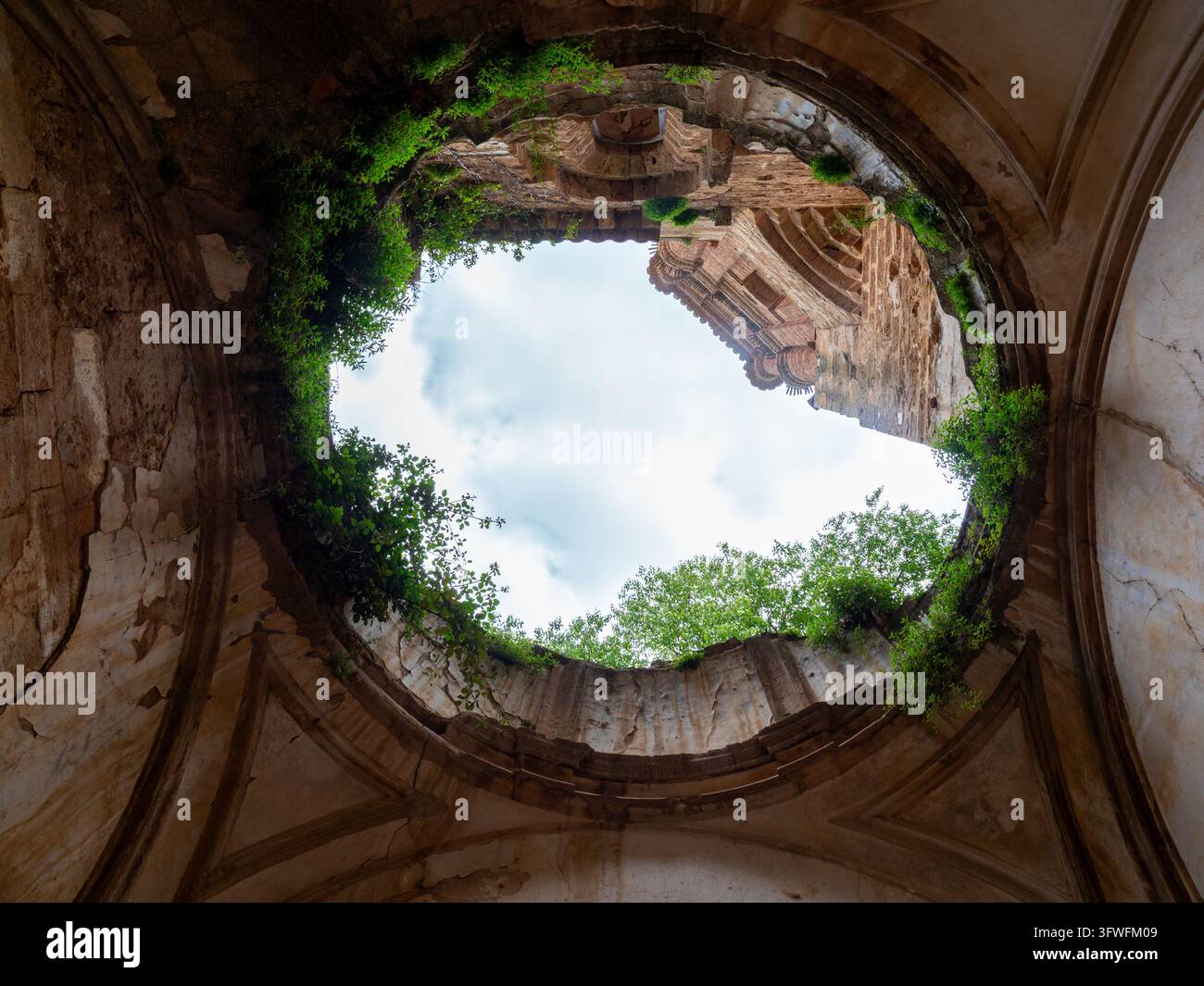 Cupola rovinata con cielo e alberi verdi - Vista dall'interno di una rovina architettonica in frantumi con un'apertura circolare in cima che rivela un verde vibrante tr Foto Stock