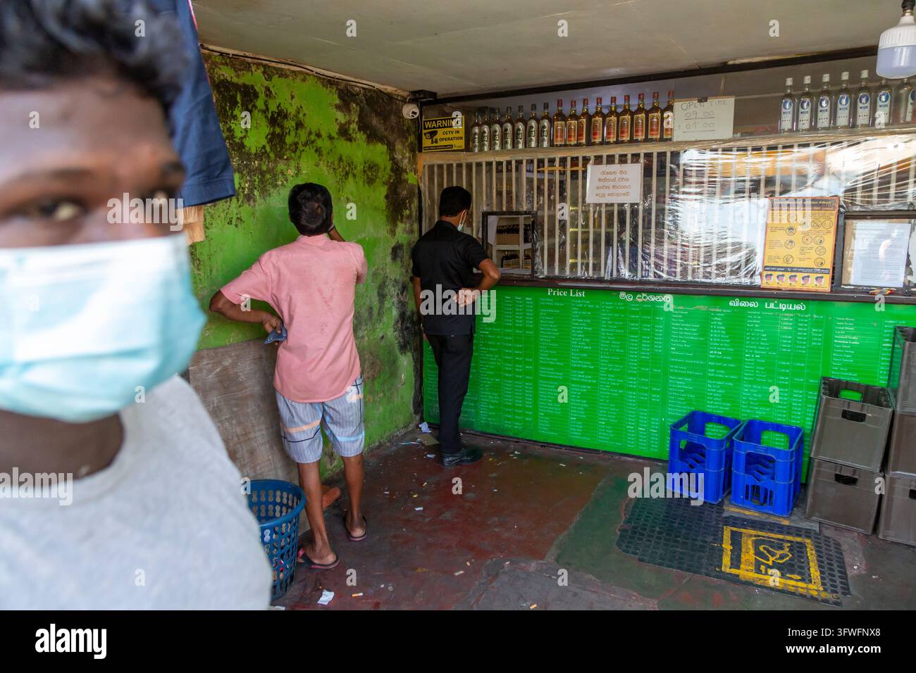 Due uomini che acquistano al bancone sbarrato di un negozio di alcolici, Provincia Occidentale, Colombo, Sri Lanka Foto Stock