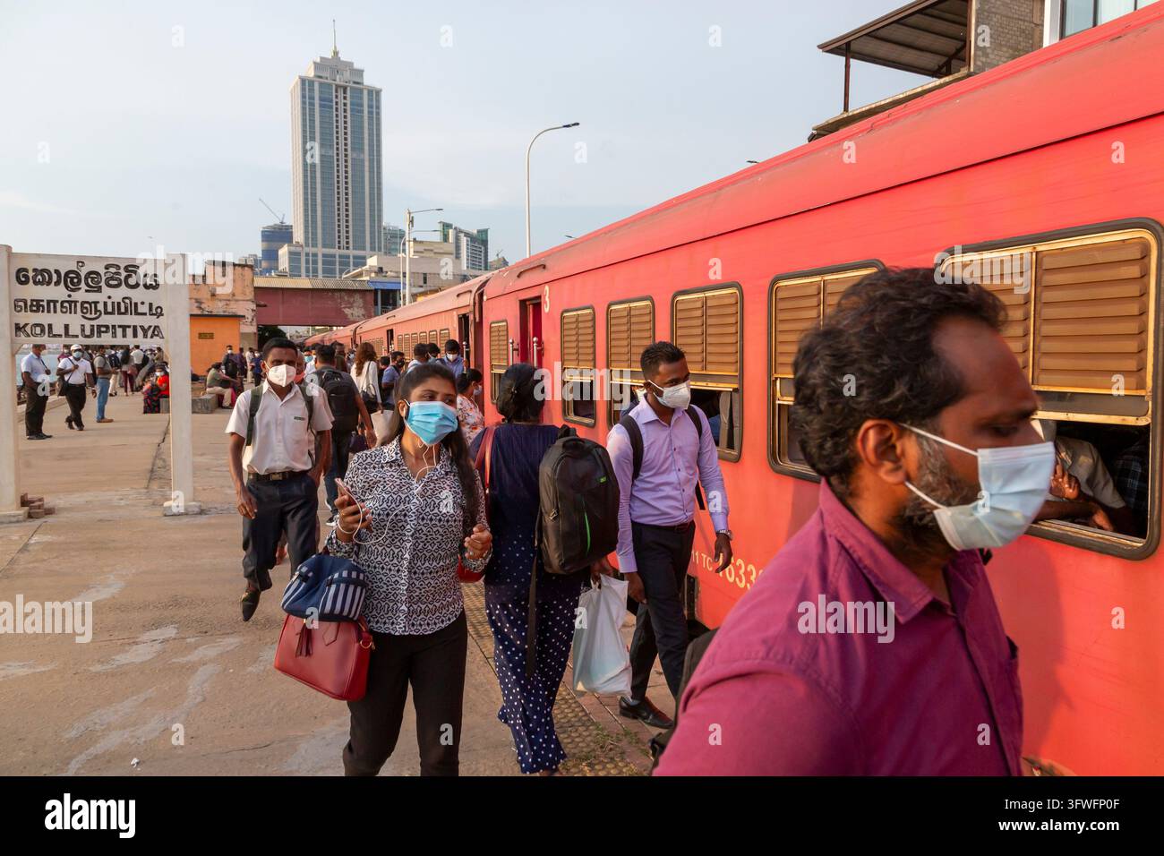 Pendolari con mascherine facciali camminano su un binario accanto a un treno rosso, Provincia Occidentale, Colombo, Sri Lanka Foto Stock