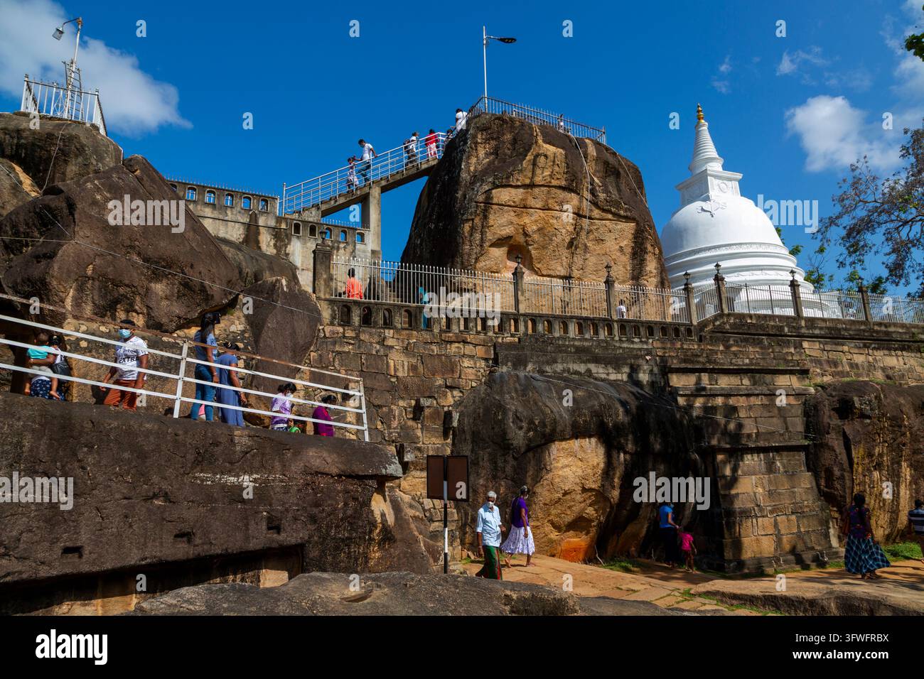 Visitatori che scalano rocce e scale al tempio di Isurumuniya con uno stupa bianco, Provincia del Nord Centro, Anuradhapura, Sri Lanka Foto Stock