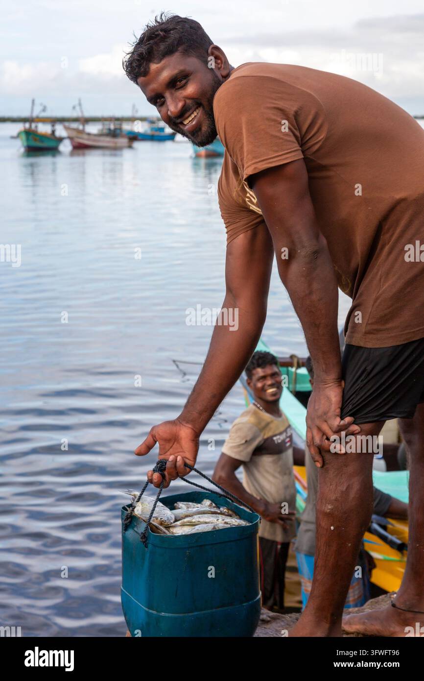 Pescatore sorridente che solleva un secchio di pesci a un molo della laguna, Provincia Settentrionale, Jaffna, Sri Lanka Foto Stock