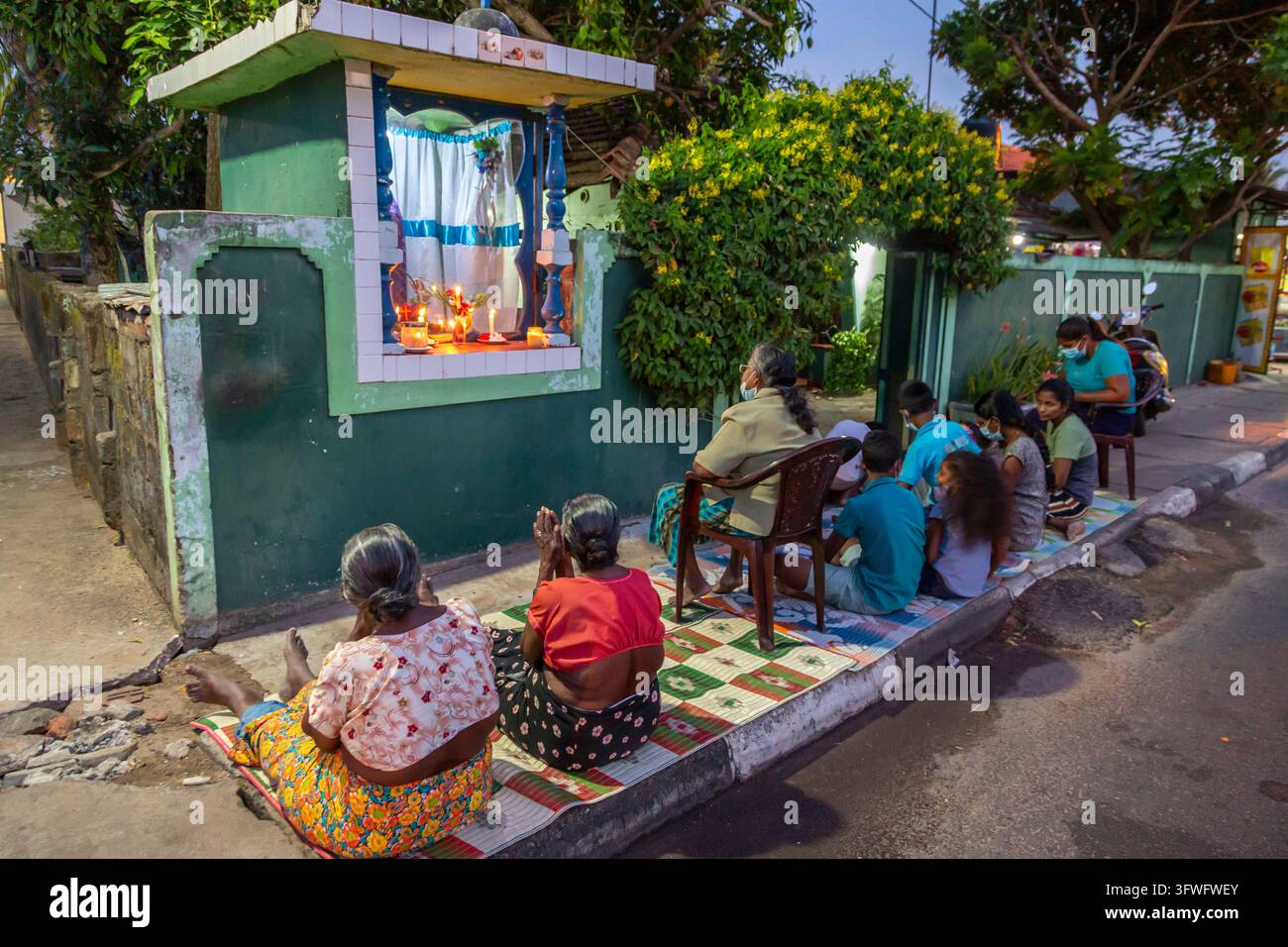 Famiglie in preghiera su stuoie davanti a un santuario stradale cristiano, Provincia occidentale, Negombo, Sri Lanka Foto Stock