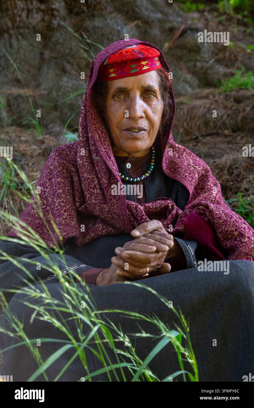 Anziana donna Gujjar con cappello rosso e scialle marrone seduta nell'erba, Jammu e Kashmir, valle di Aru, India Foto Stock