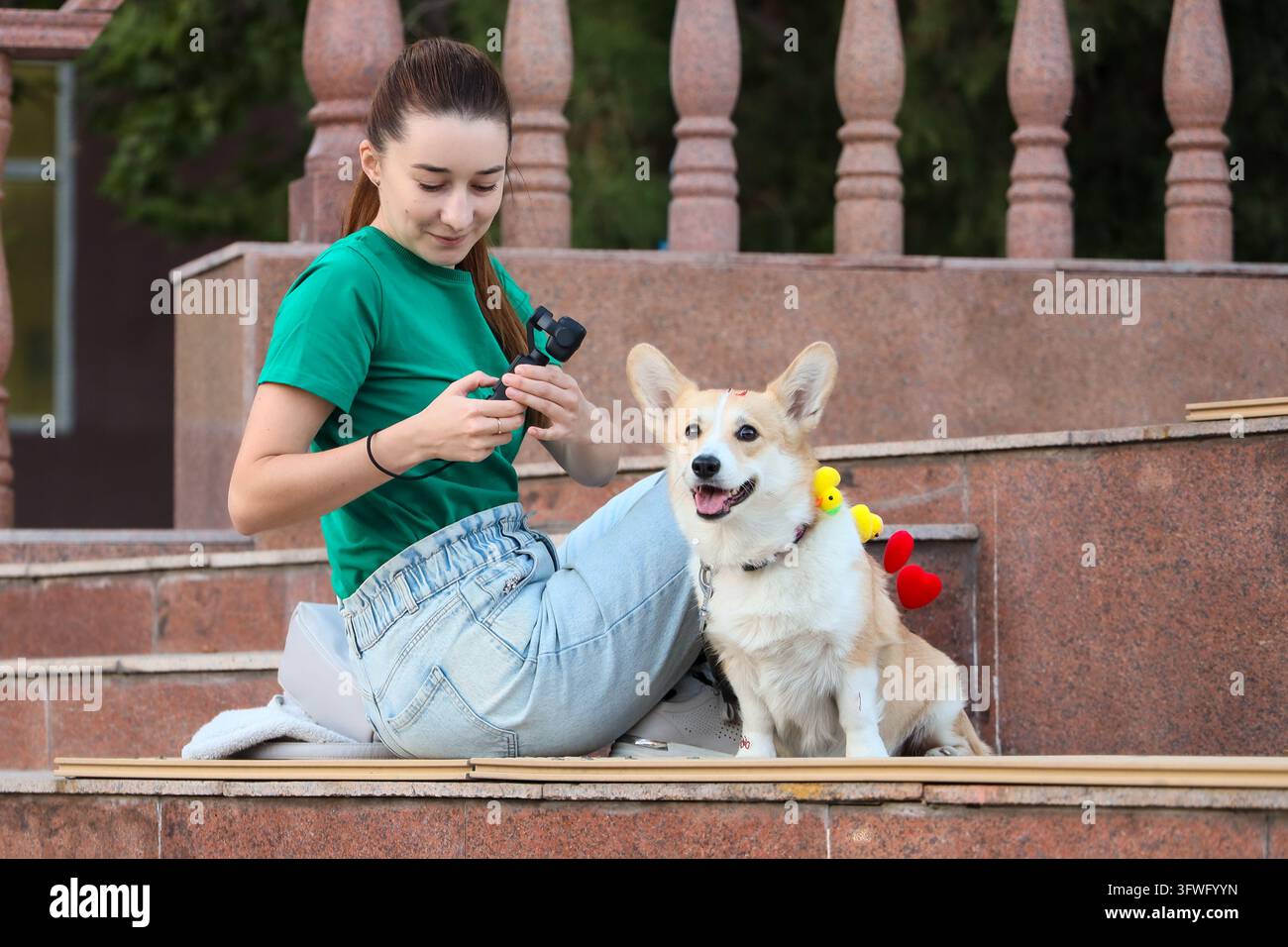 Donna che utilizza una fotocamera gimbal portatile per filmare il suo cane Pembroke Welsh Corgi all'aperto, catturando momenti di animali domestici per i social media e la creazione di contenuti digitali Foto Stock