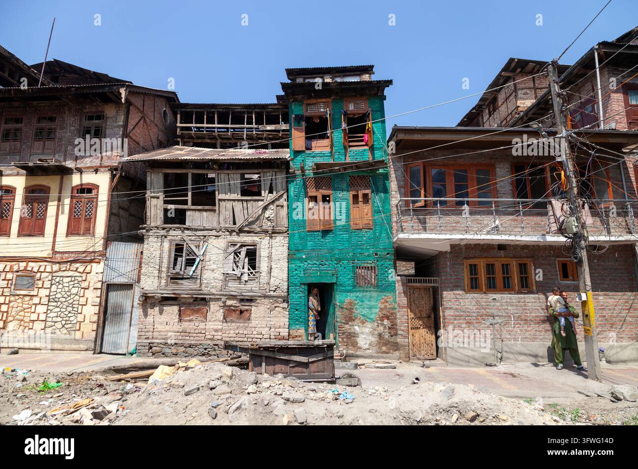 Filera di vecchie case in mattoni e legno con una facciata dipinta di verde lungo una strada polverosa, Jammu e Kashmir, Srinagar, India Foto Stock