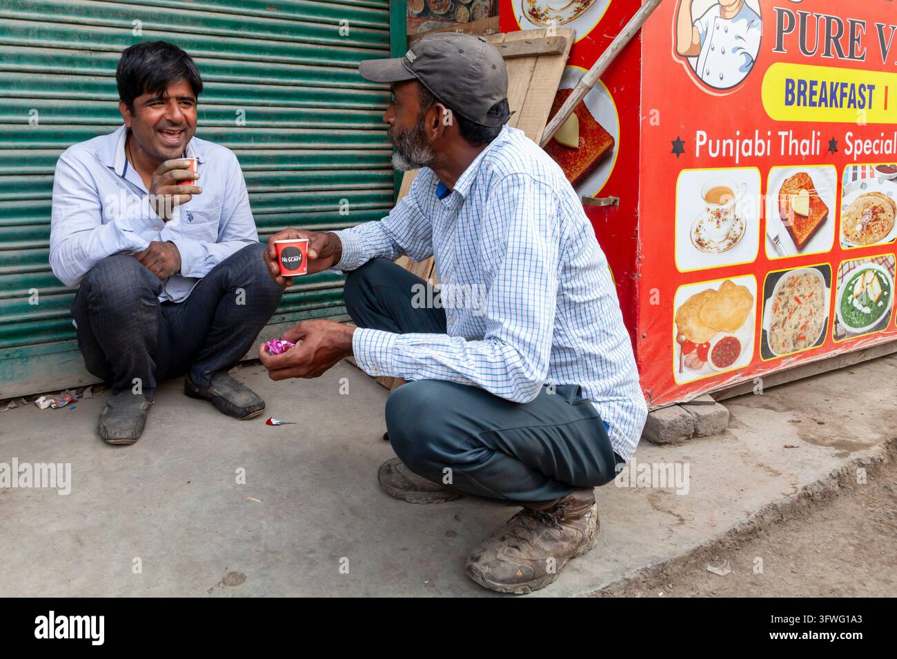 Due uomini che ridono e bevono tè mentre sono accovacciati su un marciapiede, Jammu e Kashmir, Srinagar, India Foto Stock
