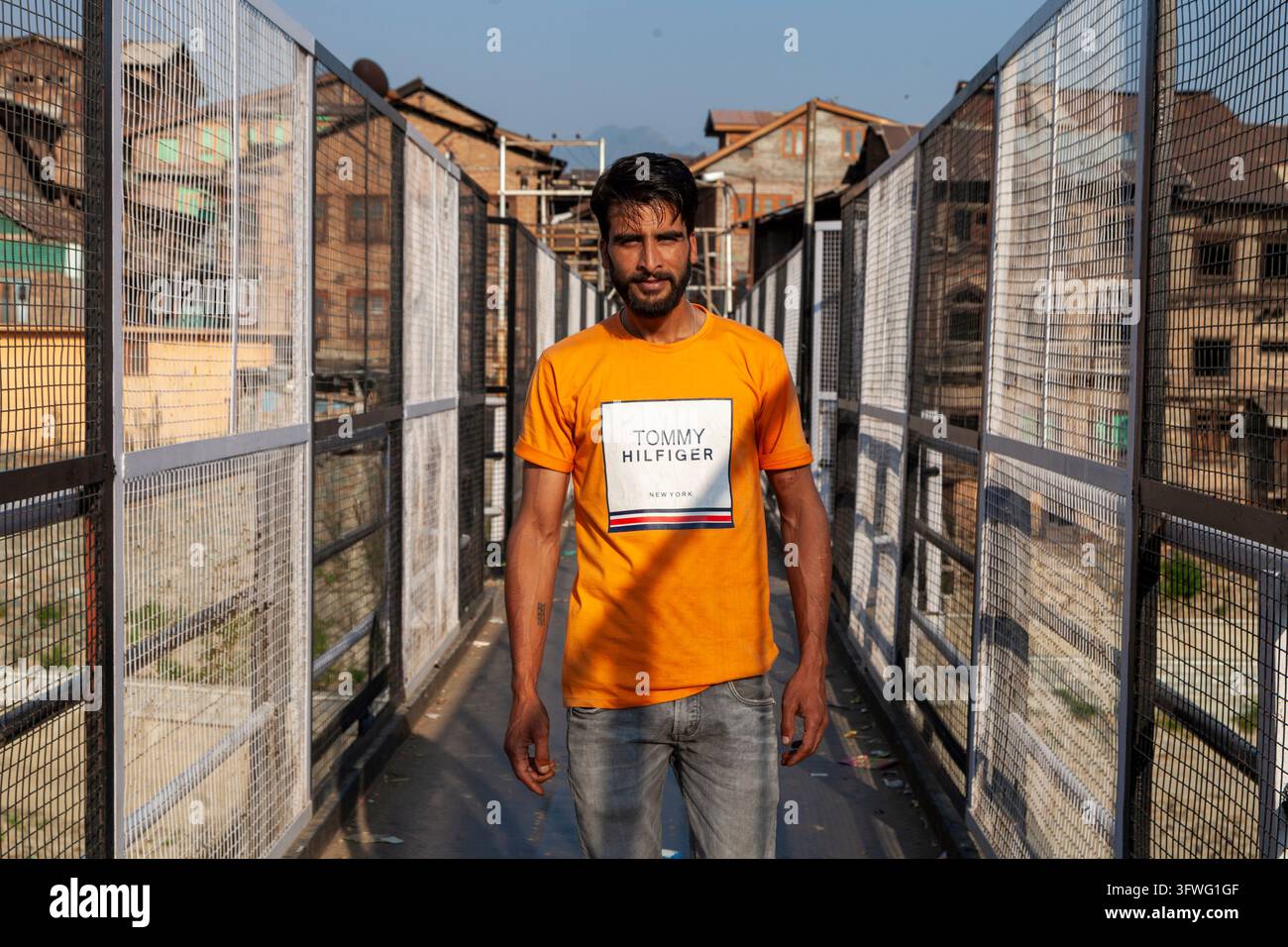 Giovane uomo in una maglietta arancione in piedi su un ponte pedonale recintato, Jammu e Kashmir, Srinagar, India Foto Stock