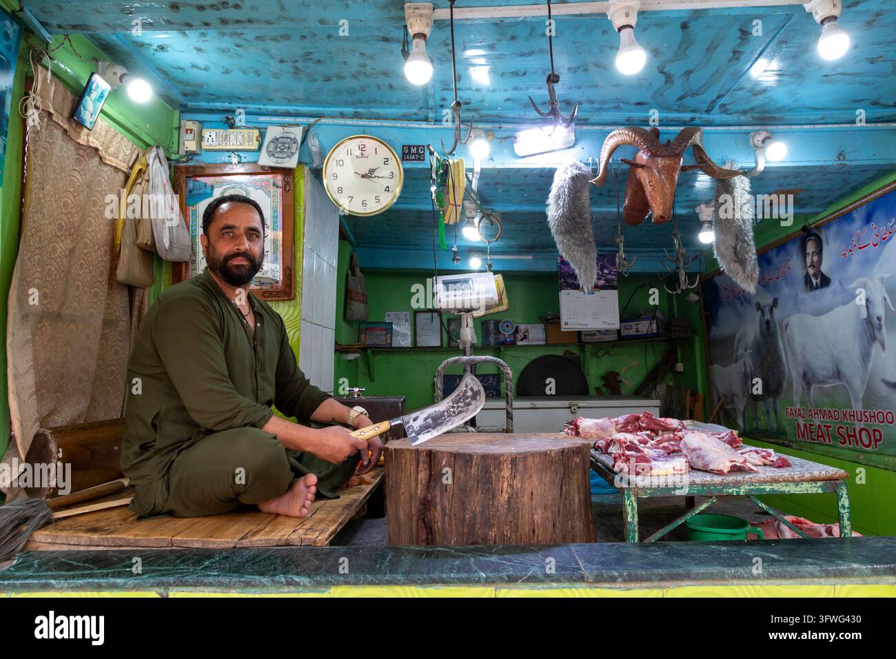 Macellaio seduto con un mannaia nella sua macelleria accanto a un blocco di taglio in legno, Jammu e Kashmir, Srinagar, India Foto Stock
