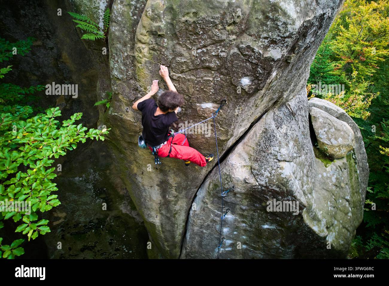 Arrampicatore avventuroso negozia una stretta chimera di roccia su un massiccio masso, mostrando resistenza, precisione e sicurezza in un ambiente forestale selvaggio Foto Stock
