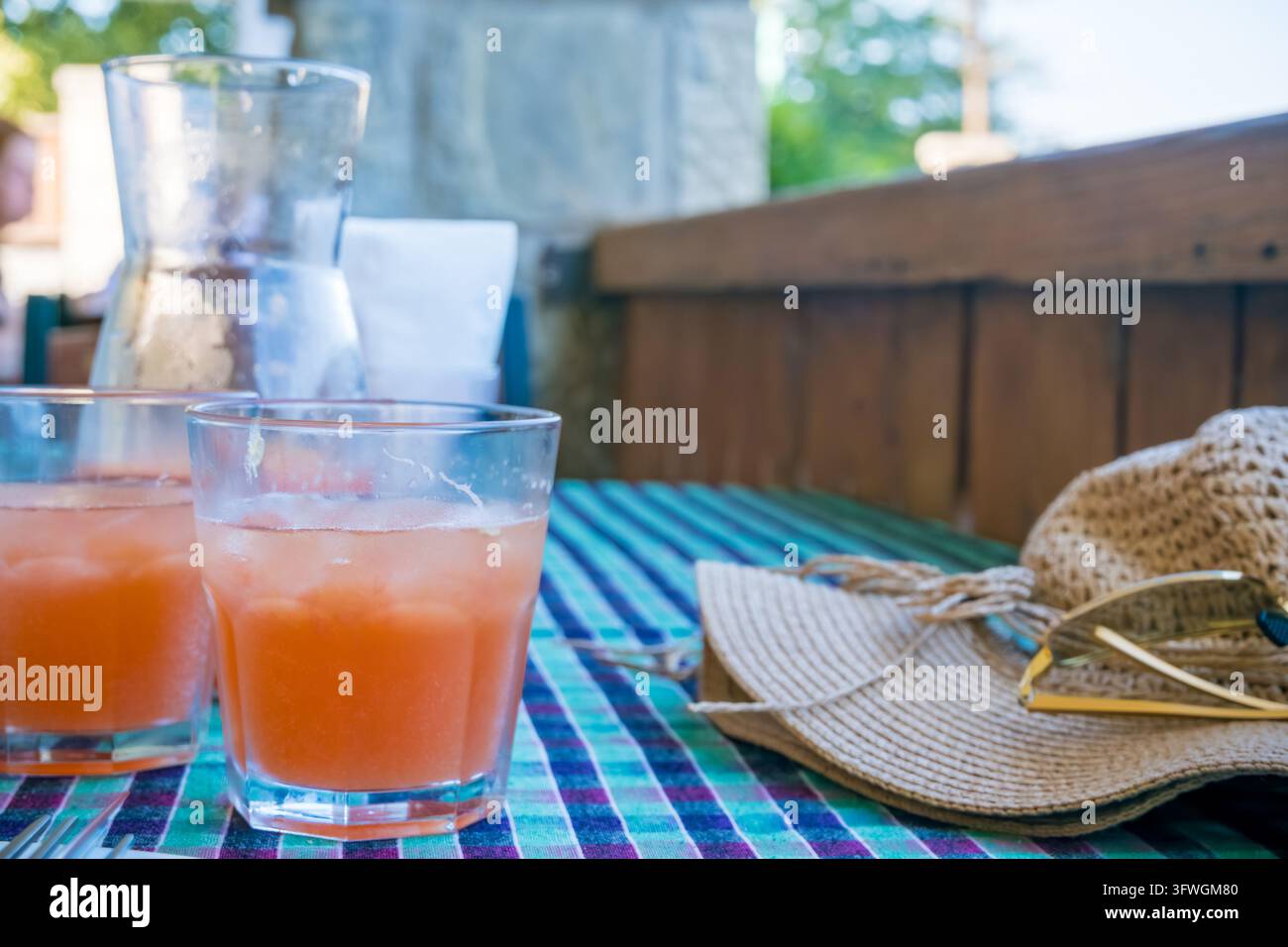 Limonata rosa in bicchieri trasparenti su una tovaglia a quadri colorata con tovaglioli tessuti e posate, disposti accanto a una finestra illuminata dal sole Foto Stock