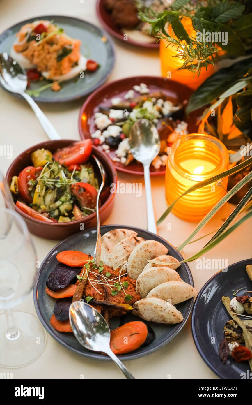 Una vista ravvicinata di più piatti con cucina mediterranea, tra cui insalate e pane, disposti su un tavolo illuminato dalla luce calda delle candele. Foto Stock