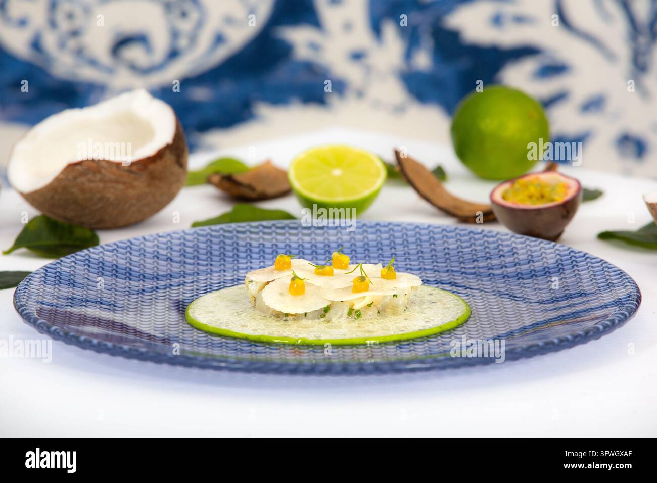 Antipasto di frutti di mare gourmet guarnito con lime, noci di cocco e semi di frutto della passione su uno sfondo blu e bianco. Foto Stock