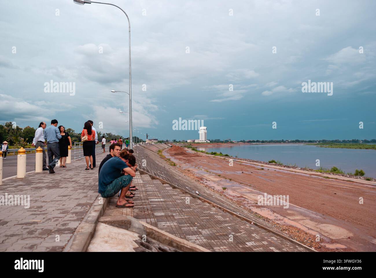 VIENTIANE, LAOS - 21 LUGLIO 2011: La gente si raduna lungo la passeggiata del Mekong a Vientiane, Laos, sotto drammatiche nuvole di monsone, riflettendo ognid Foto Stock