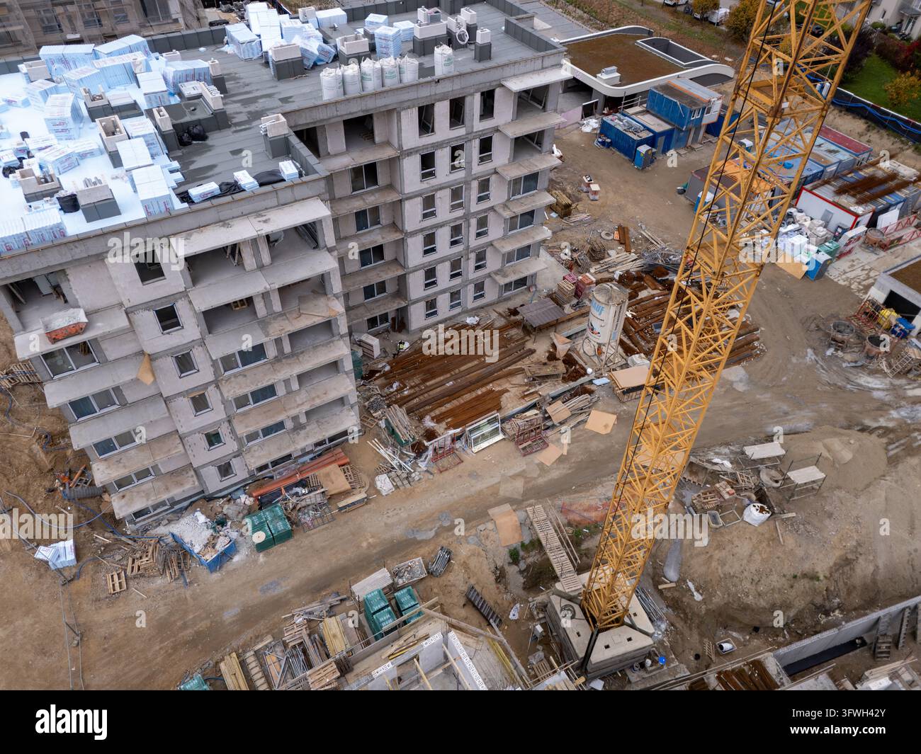 Vista aerea di un edificio in costruzione con una gru torre alta e gialla, pile di materiali isolanti sul tetto e forniture edili sul Foto Stock