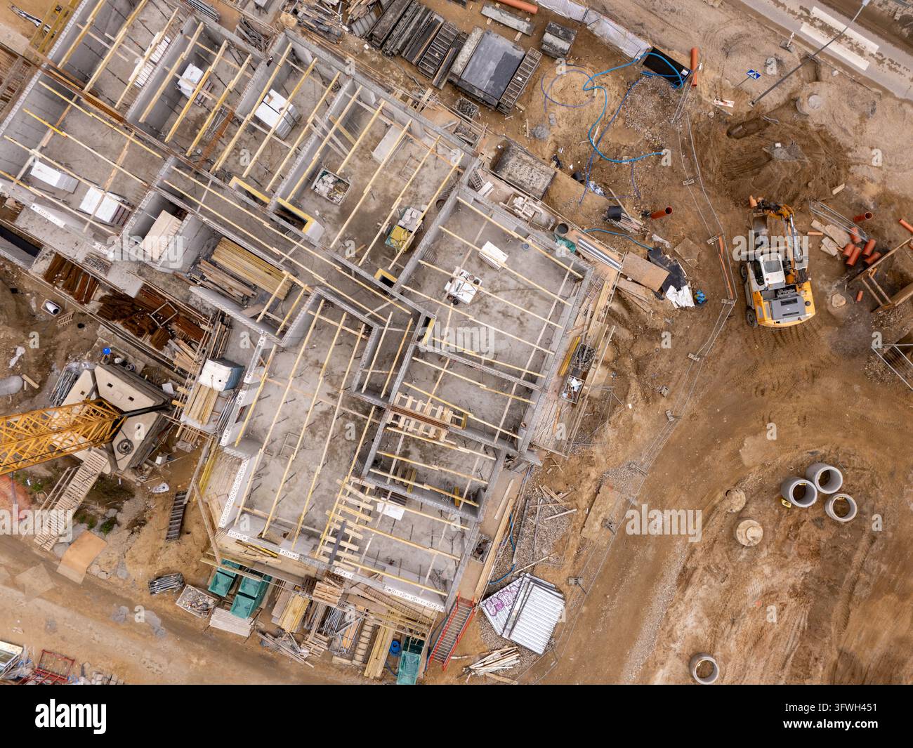 Veduta aerea di un cantiere edile con struttura in cemento, travi del tetto in legno, escavatore giallo e materiali da costruzione a Danzica, Polonia. Foto Stock