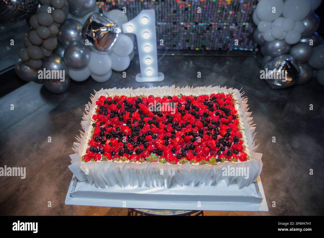 Delizioso dolce rettangolare per compleanno ricoperto di lamponi e more freschi a una prima festa di compleanno. Allestimento festoso con decorazione a palloncini Foto Stock