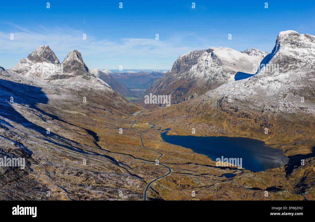 Vista aerea della tortuosa strada di montagna Trollstigen con i picchi Kongen e Alnestinden, un lago blu profondo e un terreno aspro e innevato ad Andalsnes Foto Stock